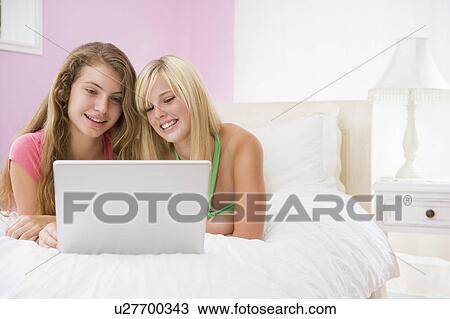 Stock Image - Teenage Girls Lying On Bed Using Laptop. Fotosearch