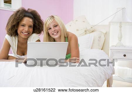 Stock Image - Teenage Girls Lying On Bed Using Laptop . Fotosearch
