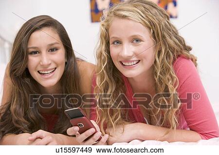 Stock Photo - Teenage Girls Lying On Bed Using Mobile Phone. Fotosearch