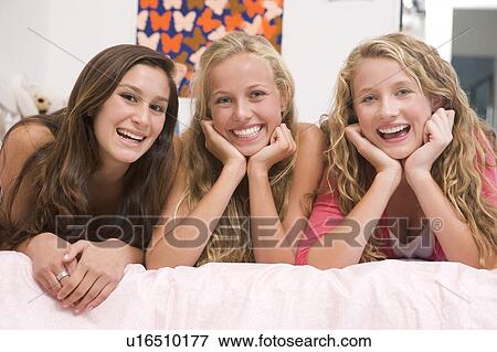 Stock Photo - Teenage Girls Lying On Bed Using Mobile Phone. Fotosearch