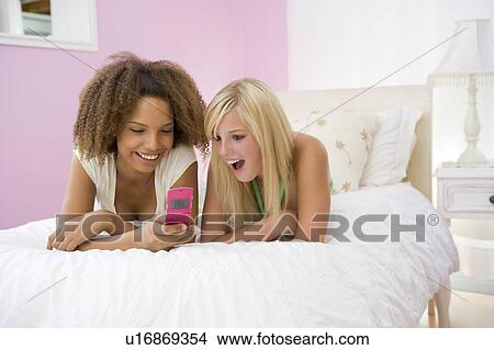 Teenage Girls Lying On Bed Using Cellphone View Large Photo Image Picture - Teenage Girls Lying On Bed Using Cellphone . Fotosearch