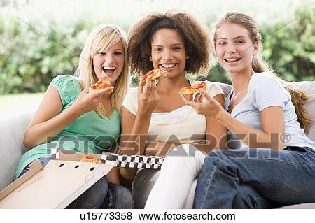 Stock Photo - Teenage Girls Sitting On Couch And Eating Pizza Together. Fotosearch