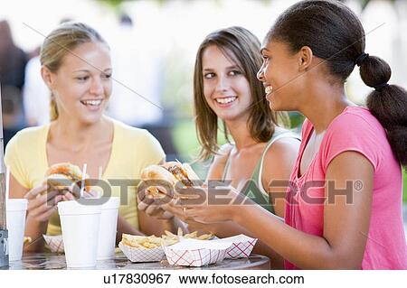 Stock Photo - Teenage Girls Sitting Outdoors Eating Fast Food . Fotosearch