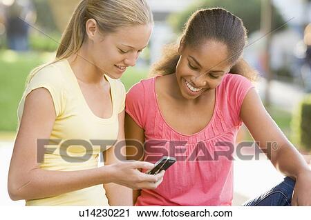 Teenage Girls Sitting Outside Playing With Mobile Phone View Large Photo Image Stock Image - Teenage Girls Sitting Outside Playing With Mobile Phone. Fotosearch
