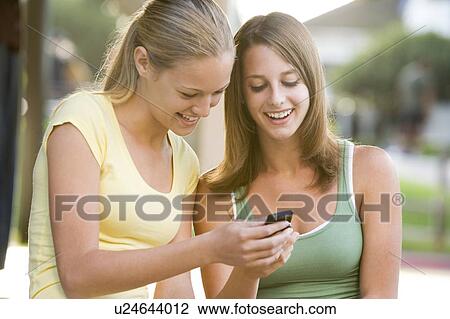 Stock Image - Teenage Girls Sitting Outside Playing With Mobile Phone. Fotosearch
