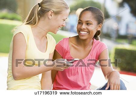 Teenage Girls Sitting Outside Playing With Mobile Phone View Large Photo Image Stock Photo - Teenage Girls Sitting Outside Playing With Mobile Phone. Fotosearch