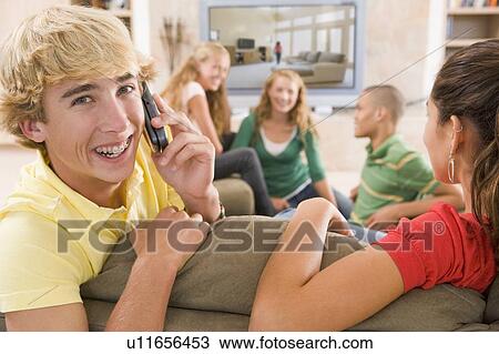 Stock Image - Teenagers Hanging Out In Front Of Television Using Mobile Phones . Fotosearch
