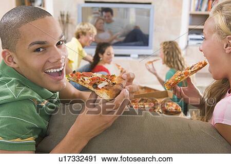 Stock Image - Teenagers Hanging Out In Front Of Television Eating Pizza . Fotosearch