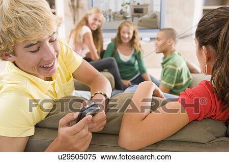 Stock Photography - Teenagers Hanging Out In Front Of Television Using Mobile Phones . Fotosearch