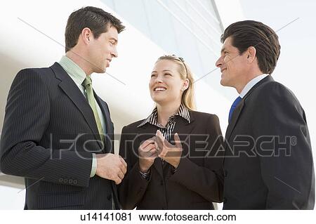 Stock Image - Three businesspeople standing outdoors by building talking and smiling. Fotosearch