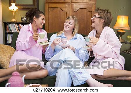 Picture - Three woman in night clothes sitting at home drinking tea. Fotosearch