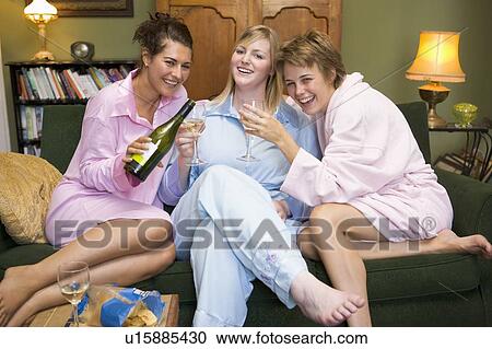 Stock Image - Three woman in night clothes sitting at home drinking wine. Fotosearch