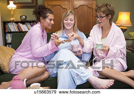 Stock Photo - Three woman in night clothes sitting at home eating cookies and drinking tea. Fotosearch