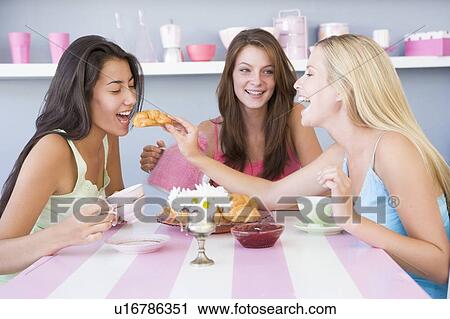 Stock Image - Three young woman sitting at a table having tea and a snack. Fotosearch