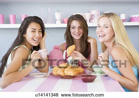 Stock Photo - Three young woman sitting at a table having tea and a snack. Fotosearch