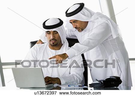 Two businessmen in office pointing at laptop (high key/selective focus) View Large Photo Image Stock Photo - Two businessmen in office pointing at laptop (high key/selective focus). Fotosearch