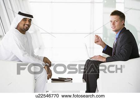 Two businessmen indoors with a laptop talking and smiling (high key/selective focus) View Large Photo Image Stock Image - Two businessmen indoors with a laptop talking and smiling (high key/selective focus). Fotosearch