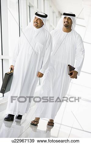 Two businessmen walking in corridor smiling (high key/selective focus) View Large Photo Image Stock Photo - Two businessmen walking in corridor smiling (high key/selective focus). Fotosearch