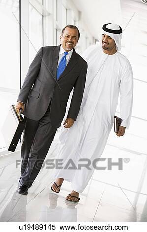 Two businessmen walking in corridor smiling (high key/selective focus) View Large Photo Image Stock Photography - Two businessmen walking in corridor smiling (high key/selective focus). Fotosearch