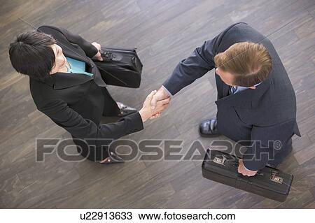 Stock Image - Two businesspeople indoors shaking hands. Fotosearch
