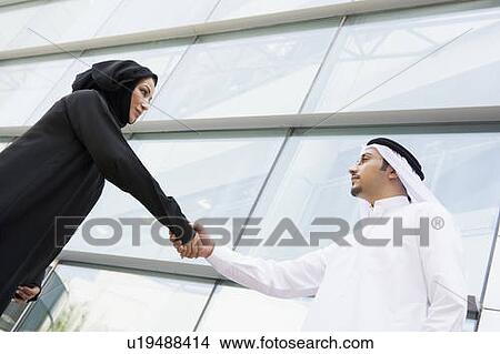 Picture - Two businesspeople outdoors by building shaking hands. Fotosearch