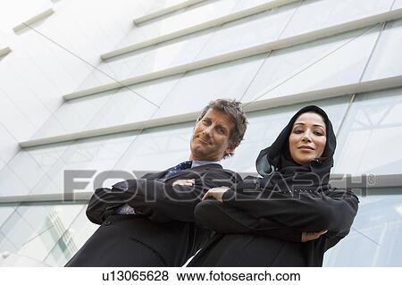Two businesspeople standing outdoors by building smiling (high key/selective focus) View Large Photo Image Stock Photo - Two businesspeople standing outdoors by building smiling (high key/selective focus). Fotosearch