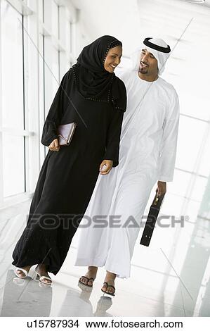 Picture - Two businesspeople walking in corridor smiling (high key/selective focus). Fotosearch