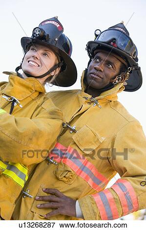 Two firefighters standing outdoors wearing helmets View Large Photo Image Stock Photo - Two firefighters standing outdoors wearing helmets. Fotosearch
