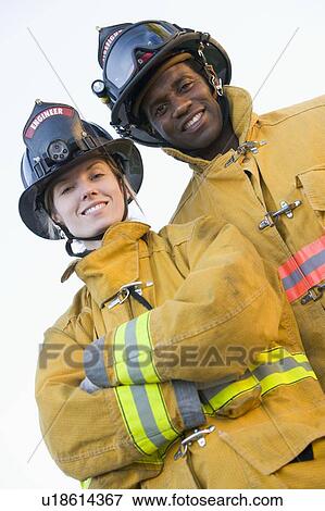 Stock Photo - Two firefighters standing outdoors wearing helmets. Fotosearch