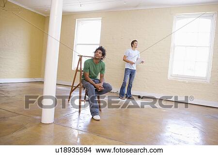 Picture - Two men in empty space with ladder holding paper. Fotosearch