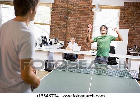 Picture - Two men in office space playing ping pong. Fotosearch