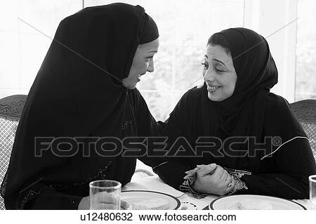 Stock Image - Two women sitting at dinner table smiling (high key). Fotosearch