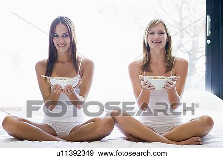 Two women sitting on bed eating cereal smiling View Large Photo Image Stock Photo - Two women sitting on bed eating cereal smiling. Fotosearch