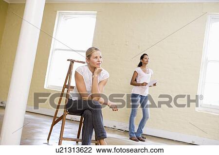 Stock Image - Two women with ladder in empty space holding paper. Fotosearch