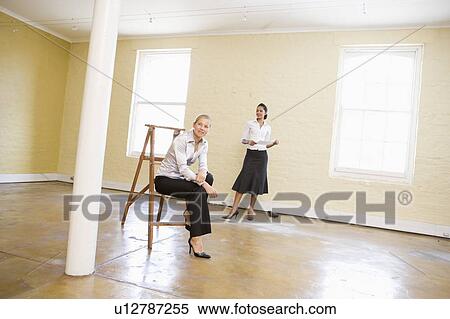 Two women with ladder in empty space holding paper smiling View Large Photo Image Stock Photography - Two women with ladder in empty space holding paper smiling. Fotosearch