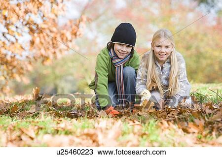 Two young children outdoors at park playing in leaves and smiling (selective focus) View Large Photo Image Stock Image - Two young children outdoors at park playing in leaves and smiling (selective focus). Fotosearch