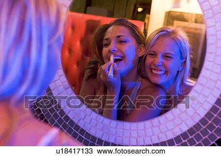Stock Image - Two young women applying makeup in a mirror. Fotosearch