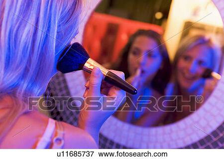 Two young women applying makeup in a mirror View Large Photo Image Stock Photo - Two young women applying makeup in a mirror. Fotosearch