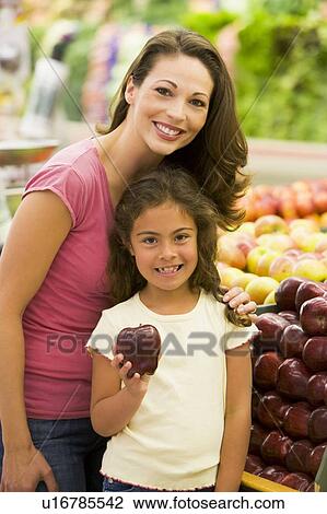 Stock Image - Woman and daughter shopping for apples at a grocery store. Fotosearch