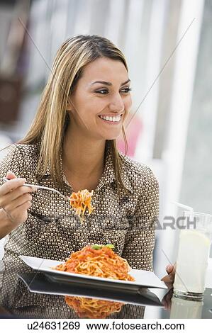 Stock Photo - Woman at restaurant eating spaghetti and smiling (selective focus). Fotosearch