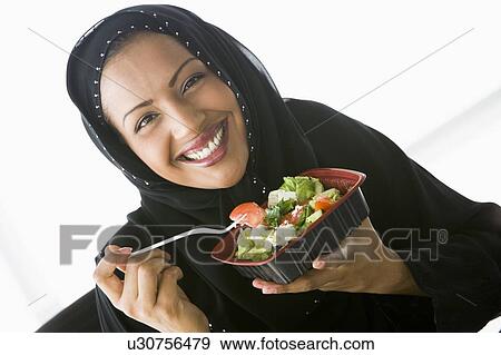 Stock Photo - Woman eating salad and smiling (high key/selective focus). Fotosearch