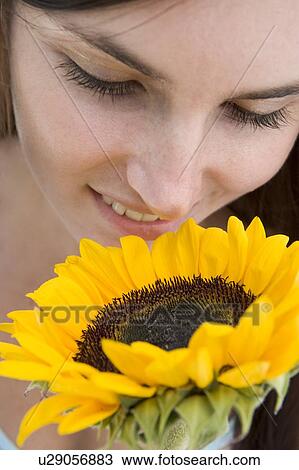 Stock Image - Woman holding and smelling a sunflower. Fotosearch