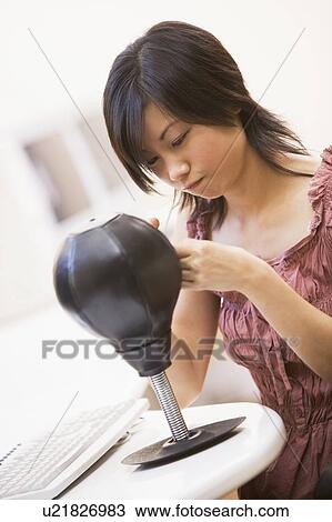 Stock Image - Woman in computer room sitting by small punching bag. Fotosearch