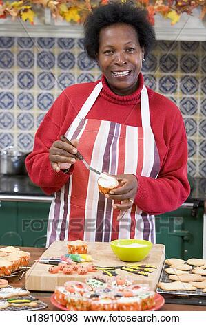 Stock Image - Woman in kitchen making Halloween treats and smiling. Fotosearch