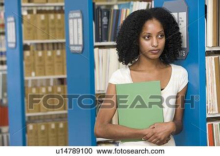 Stock Image - Woman in library holding book (depth of field). Fotosearch