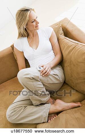 Stock Image - Woman in living room listening to MP3 player smiling. Fotosearch