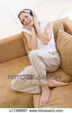 Woman in living room listening to headphones smiling View Large Photo Image Stock Photo - Woman in living room listening to headphones smiling. Fotosearch