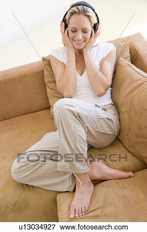 Woman in living room listening to headphones smiling View Large Photo Image Stock Photo - Woman in living room listening to headphones smiling. Fotosearch