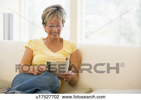 Woman in living room reading book smiling View Large Photo Image Stock Image - Woman in living room reading book smiling. Fotosearch