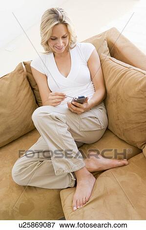 Stock Photo - Woman in living room using personal digital assistant smiling. Fotosearch